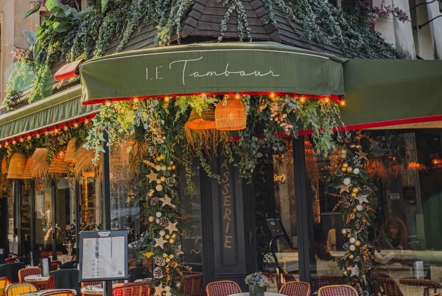 Le Tambour brasserie entrance decorated with hanging plants, wicker lamps, and festive garlands with pinecones and gold ornaments.