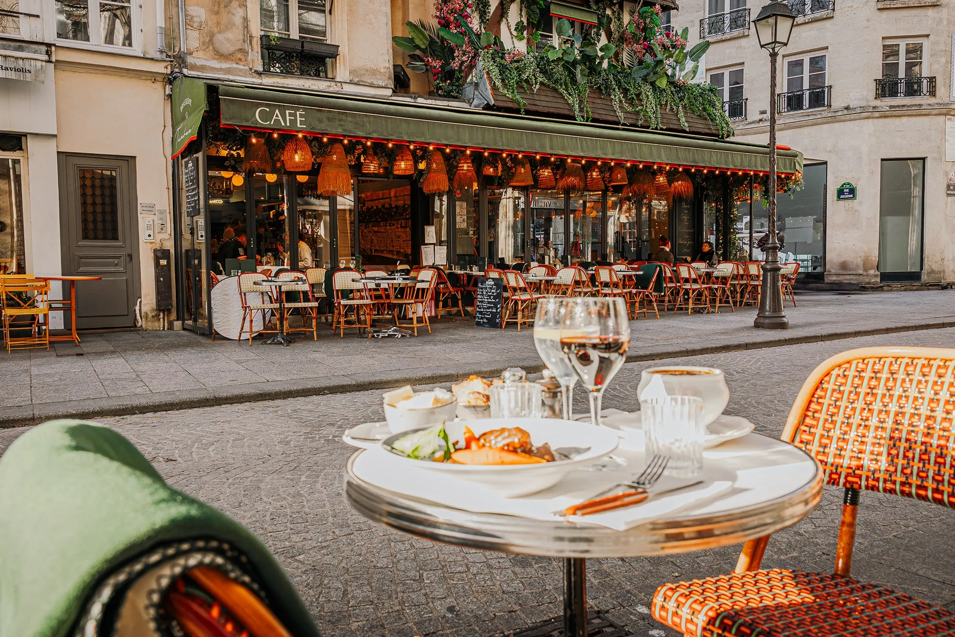Outdoor café seating with tables and chairs, featuring a table in the foreground set with plates, glasses, and cutlery on a cobblestone street.