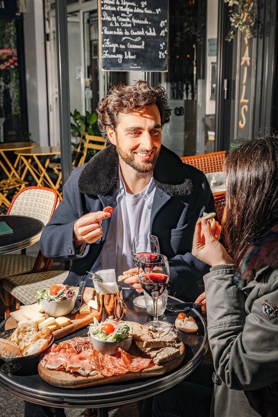Couple enjoying a charcuterie board with bread, cheese, salad, and two glasses of red wine at an outdoor café.